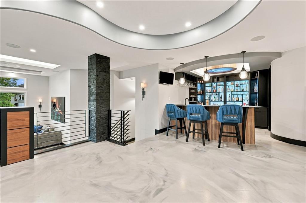 Modern home bar with blue stools, lit bottle shelves, and a dark stone column.