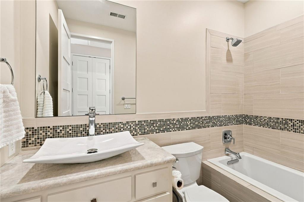 Bathroom with a vessel sink, stone countertop, and tiled bathtub with mosaic accent band.