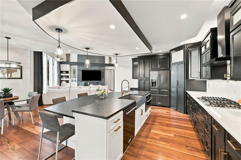 Open-plan kitchen with a large island, dark cabinets, and hardwood floors, opening to the living room.