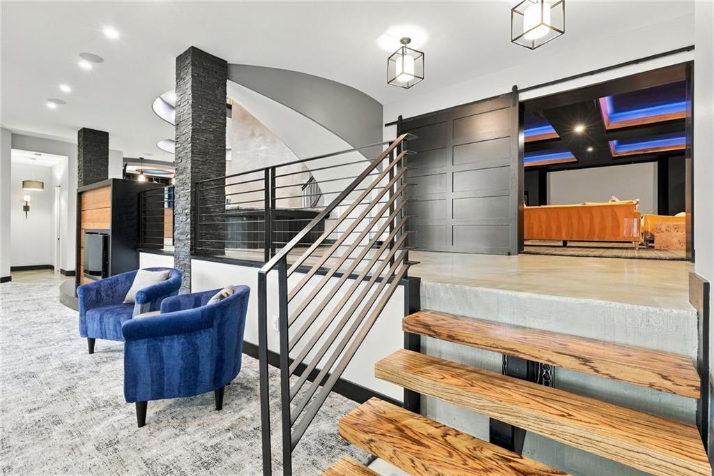 Foyer with open-riser wood staircase, black metal railings, and two blue chairs.