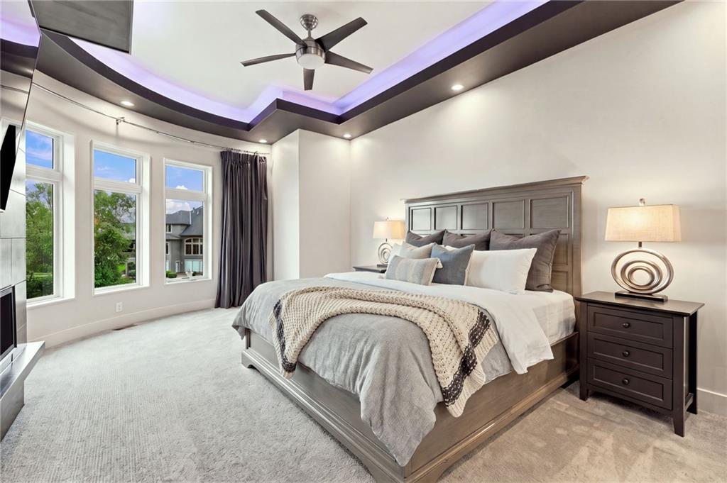 Bedroom with a gray bed, tall windows, and a tray ceiling lit with purple accents.