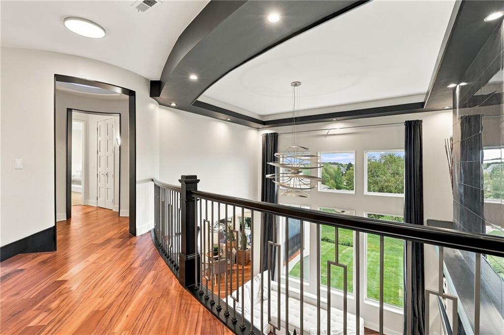 Upstairs landing overlooking a bright living area, with dark railings, hardwood floors, and tall windows.