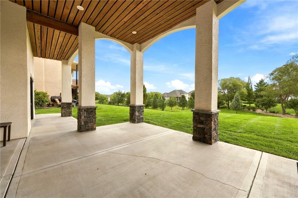 Covered patio with a wood ceiling and arched columns overlooking a green lawn.