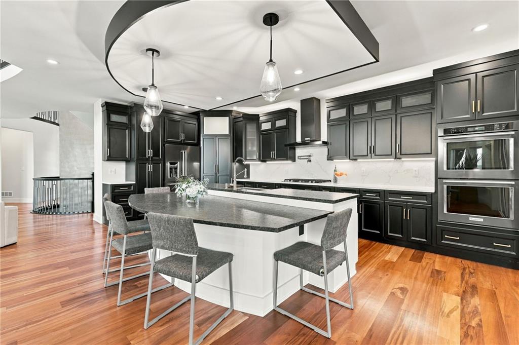 Modern kitchen with dark cabinets, a large island, pendant lights, and hardwood floors.
