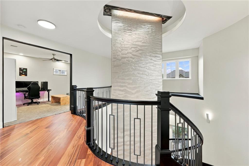 Upstairs landing with curved black railing, tall stone feature wall, hardwood floors, and an adjoining office.