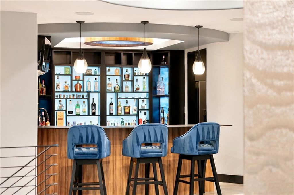 Home bar with backlit bottle shelves, a wood-front counter, and three blue upholstered stools.