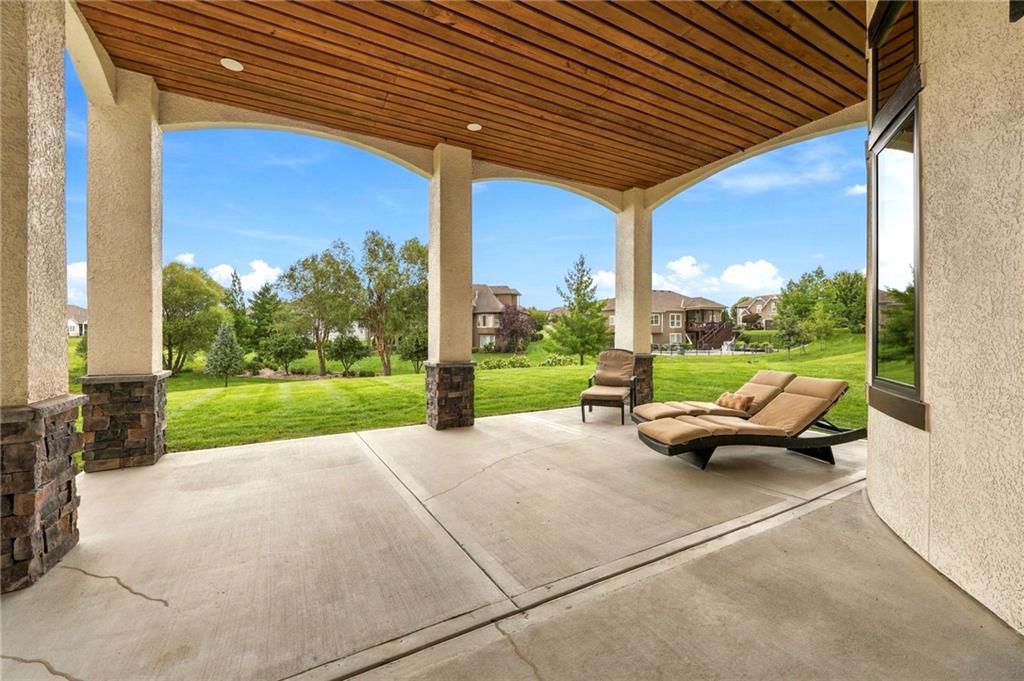 Covered patio with a wood ceiling and chaise lounges overlooking a landscaped lawn.