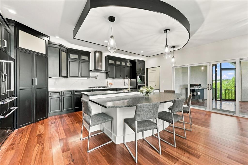 Modern kitchen with dark cabinets, a large island, pendant lights, and sliding doors to a balcony.