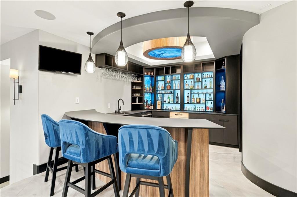 Wet bar with a curved island, blue stools, illuminated bottle shelves, and a blue-lit ceiling feature.