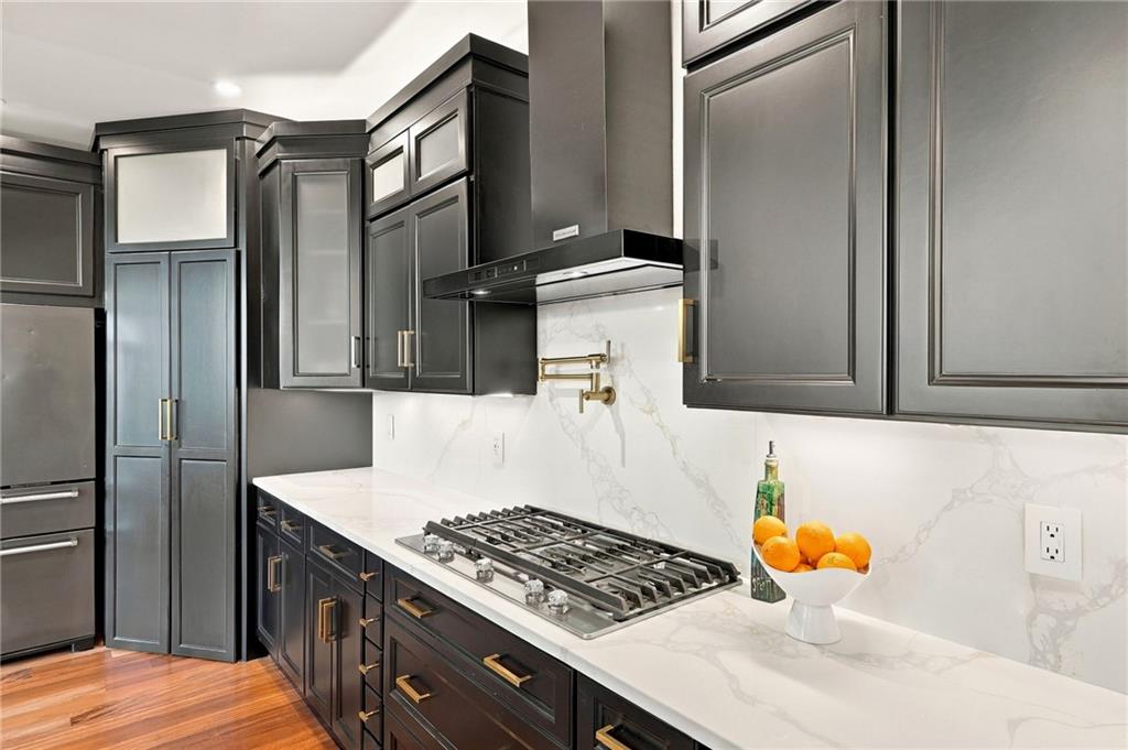Kitchen with dark cabinetry, a wide gas cooktop, and white veined stone counters.