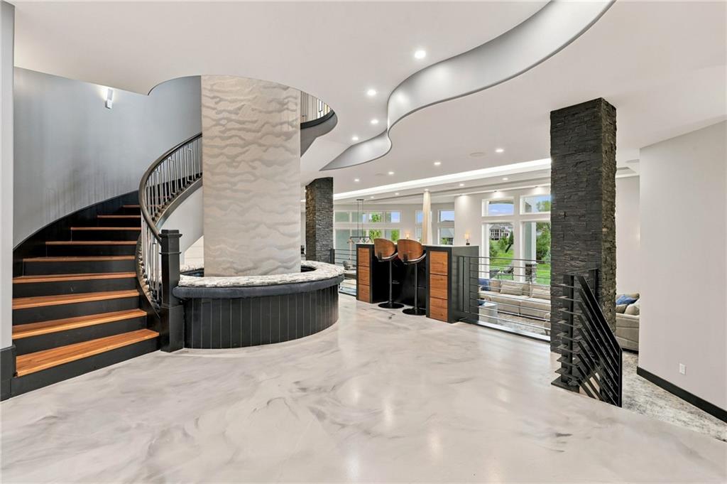 Contemporary foyer with a curved staircase, sculptural stone column, and bar overlooking large windows.
