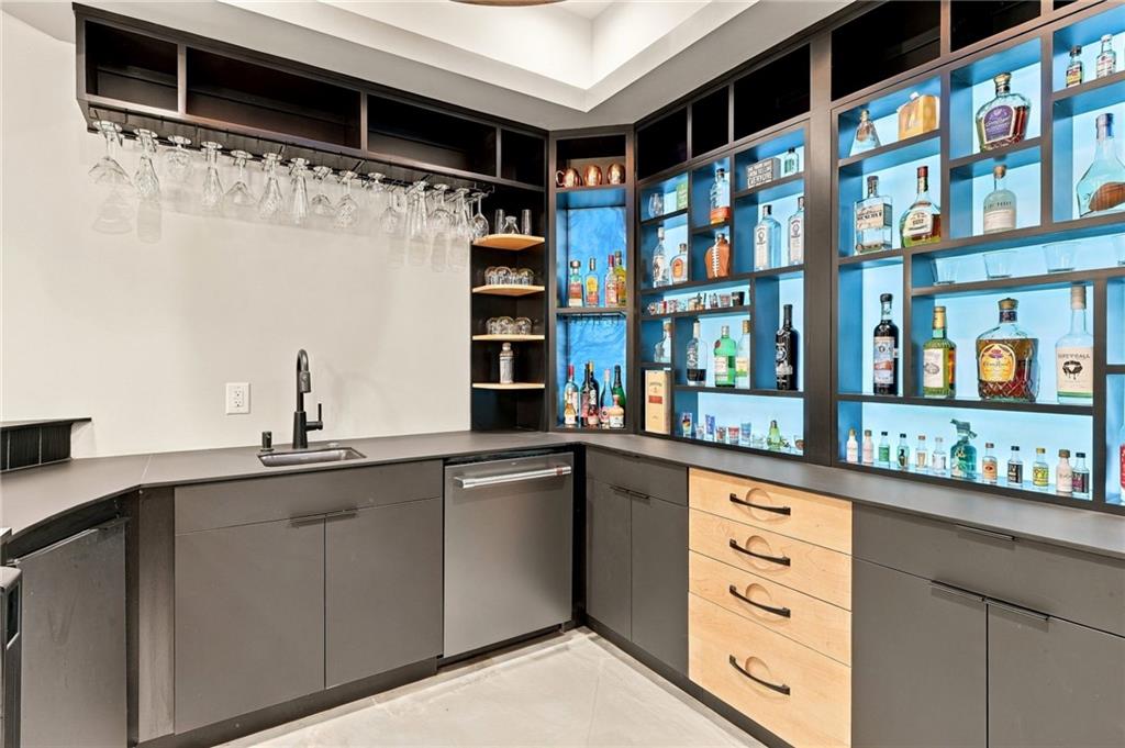 Wet bar with a sink, hanging wine glasses, and illuminated liquor display shelves.