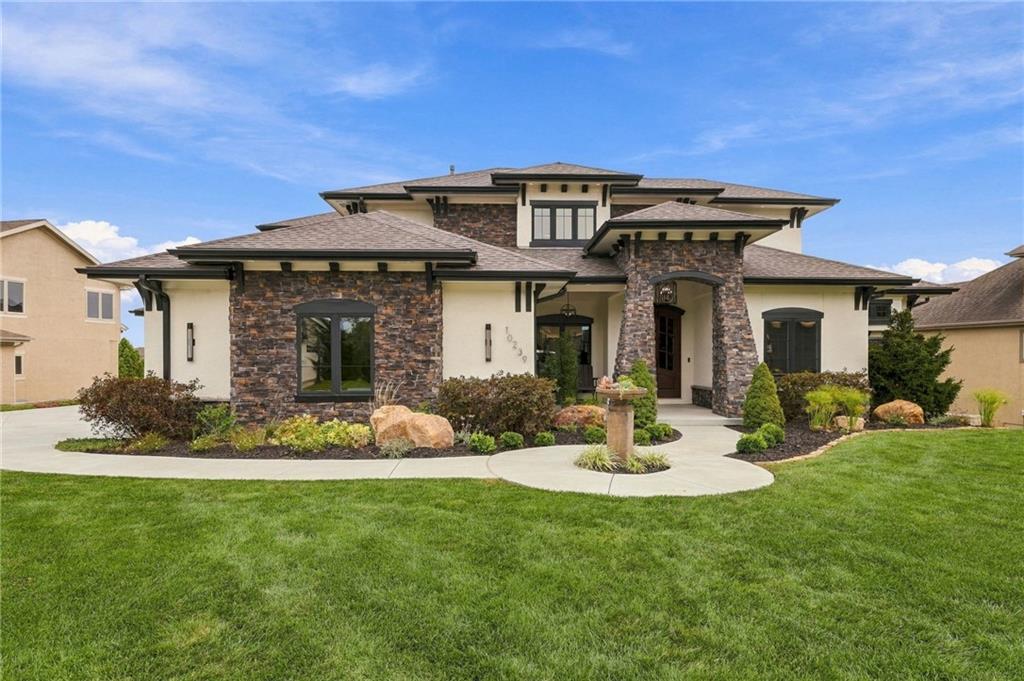 Two-story home with a stone facade, covered entry, landscaped beds, and a broad green lawn.