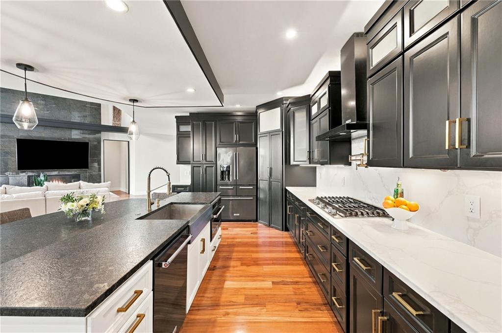 Kitchen with dark cabinets, marble-look counters, a large island, and warm wood floors.