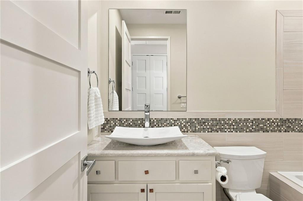 Bathroom with a white vessel sink, mosaic backsplash, and pale vanity beside a toilet.