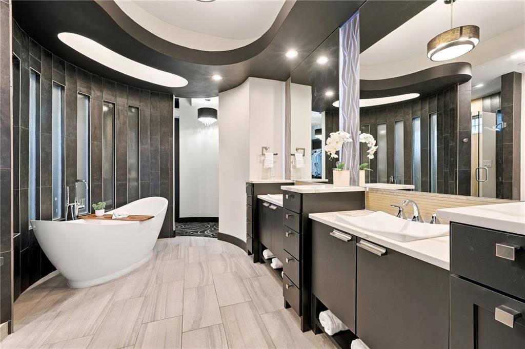 Modern bathroom with a freestanding tub, dark tile, and double vanities.