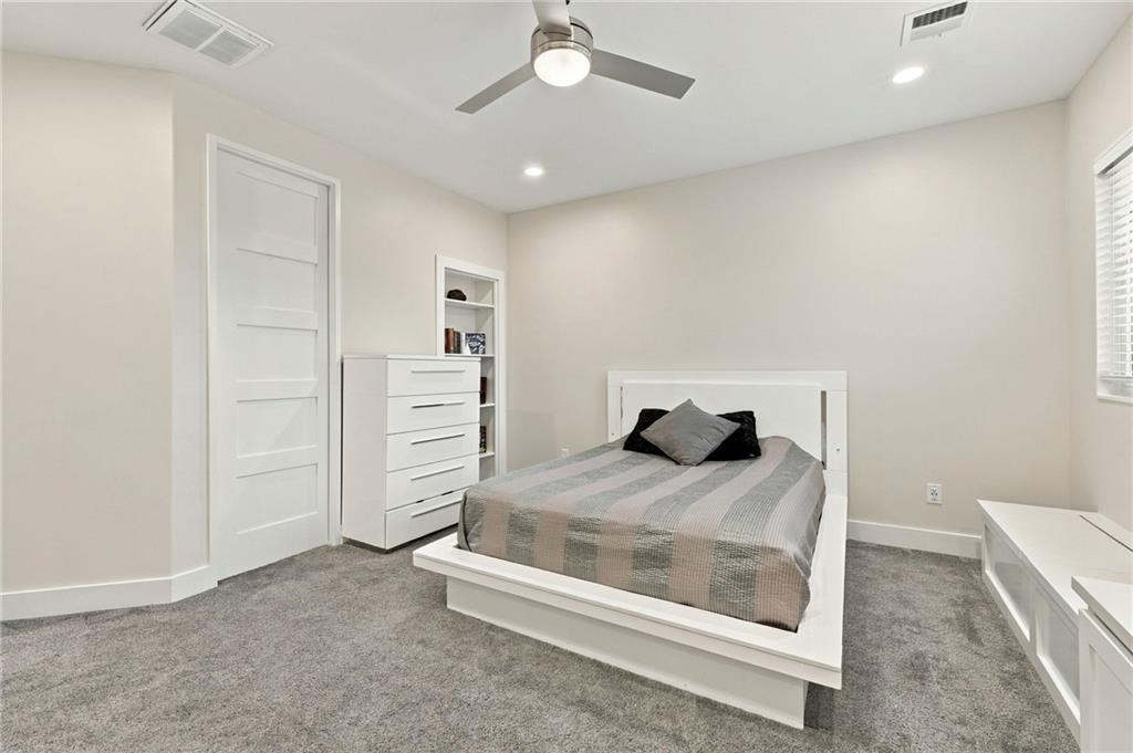 Bedroom with a white bed, gray bedding and carpet, built-in shelves, and a ceiling fan.