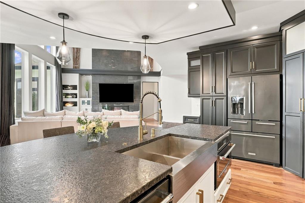 Kitchen with a large stone island, dark cabinets, stainless steel appliances, and an adjoining living area.