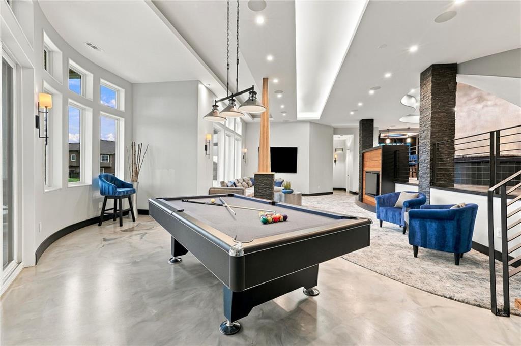 Game room with a pool table, blue lounge chairs, tall windows, and a stone fireplace.