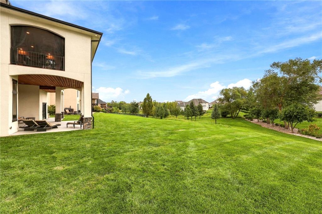Home’s covered patio overlooks a wide, manicured lawn and mature trees.
