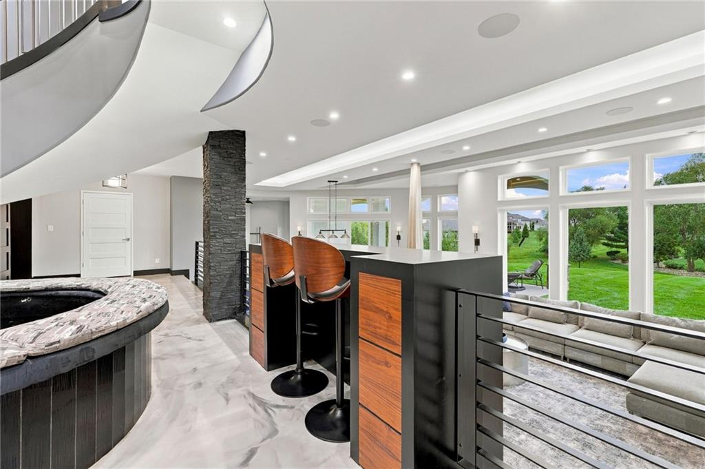 Open lounge with a raised hot tub, bar stools, and large windows overlooking a green backyard.