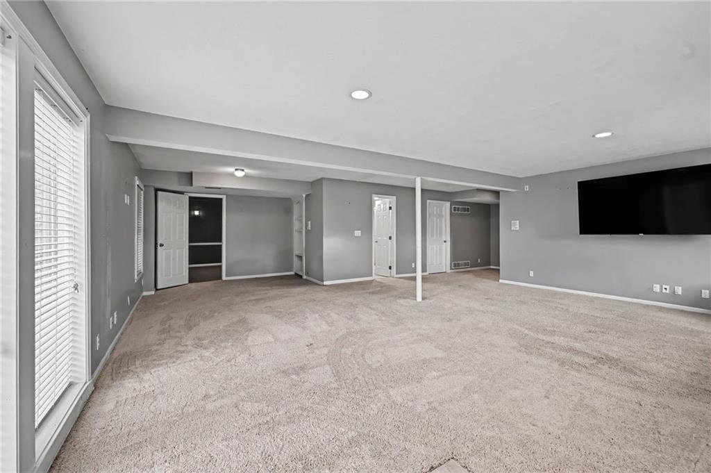 Unfurnished carpeted room with gray walls, a support post, and a wall-mounted television.