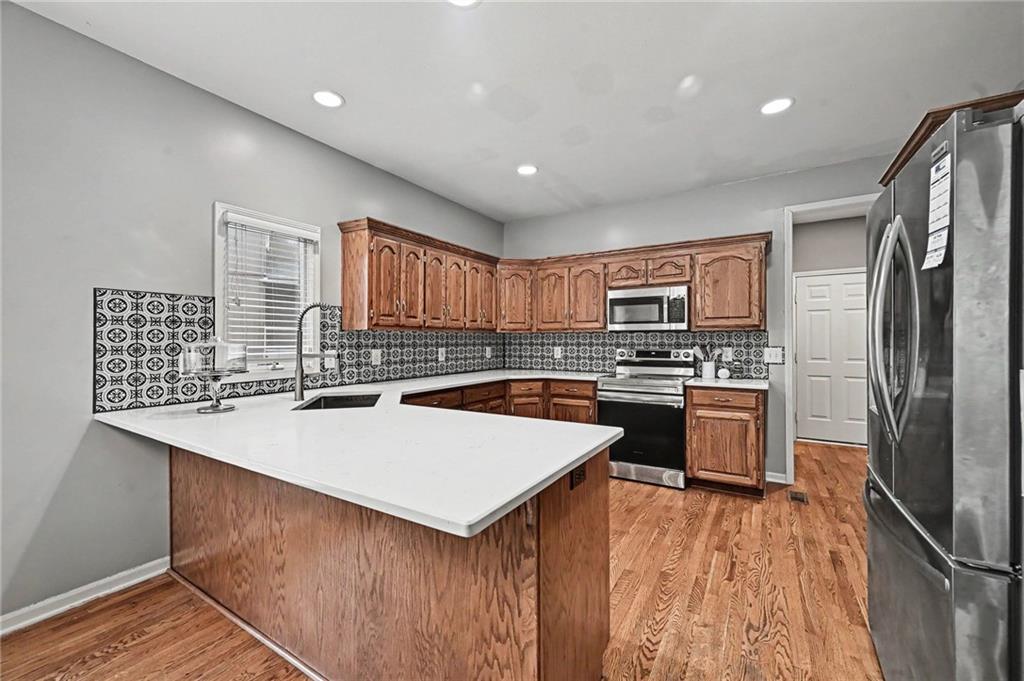 Kitchen with a white peninsula, wood cabinets, patterned tile backsplash, and stainless steel appliances.