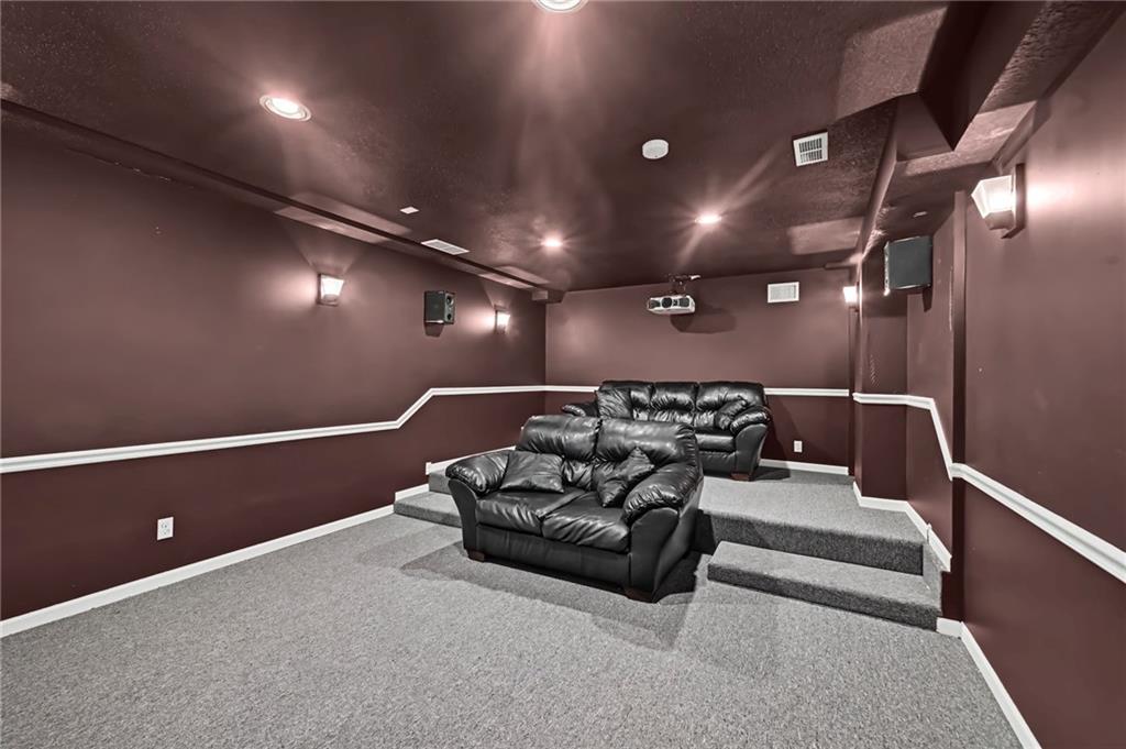 Home theater with black leather recliners, tiered platforms, and a ceiling-mounted projector.