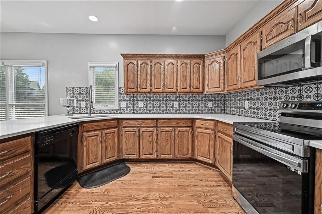 Kitchen with ornate wood cabinets, patterned tile backsplash, stainless steel appliances, and hardwood floors.