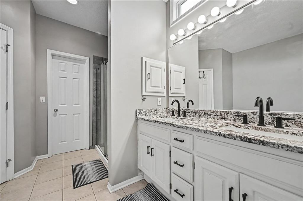Bathroom with a double vanity, granite countertop, large mirror, and glass-enclosed shower.