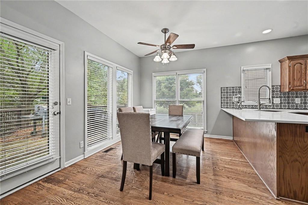 Dining area with hardwood floors, large windows, and a dark table beside the kitchen.