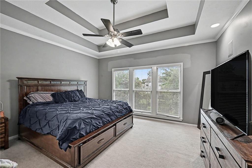 Bedroom with a dark wood bed, tray ceiling, ceiling fan, and three windows with blinds.