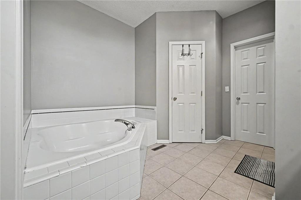 Bathroom with a large tiled soaking tub, gray walls, and beige tile flooring.