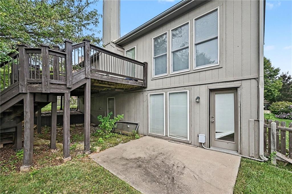 Rear of a gray-sided house with a raised wooden deck and concrete patio.