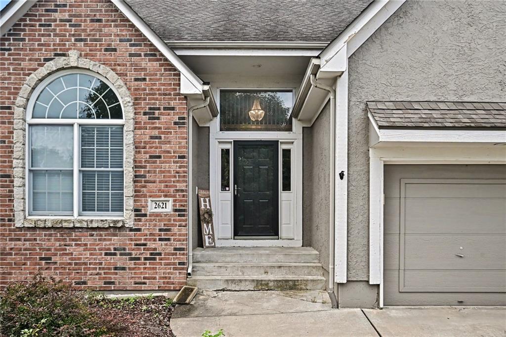 House entrance with a red brick facade, arched window, recessed front door, and attached garage.