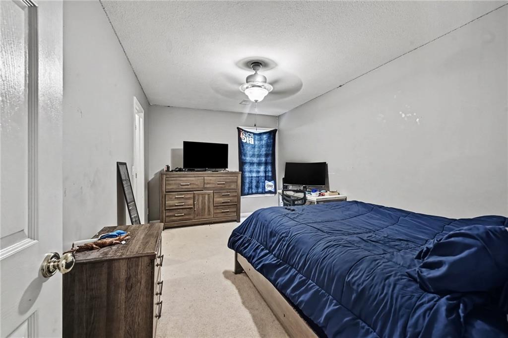 Furnished bedroom with a large blue-covered bed, wooden dresser, television, and ceiling fan.