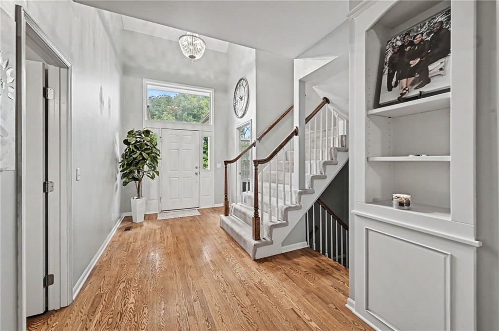 Entry foyer with hardwood floors, a carpeted staircase, and a white front door beneath a large transom window.