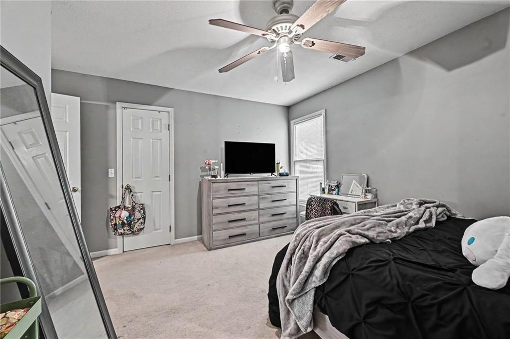 Bedroom with a black bed, gray throw, dresser and TV, and ceiling fan.