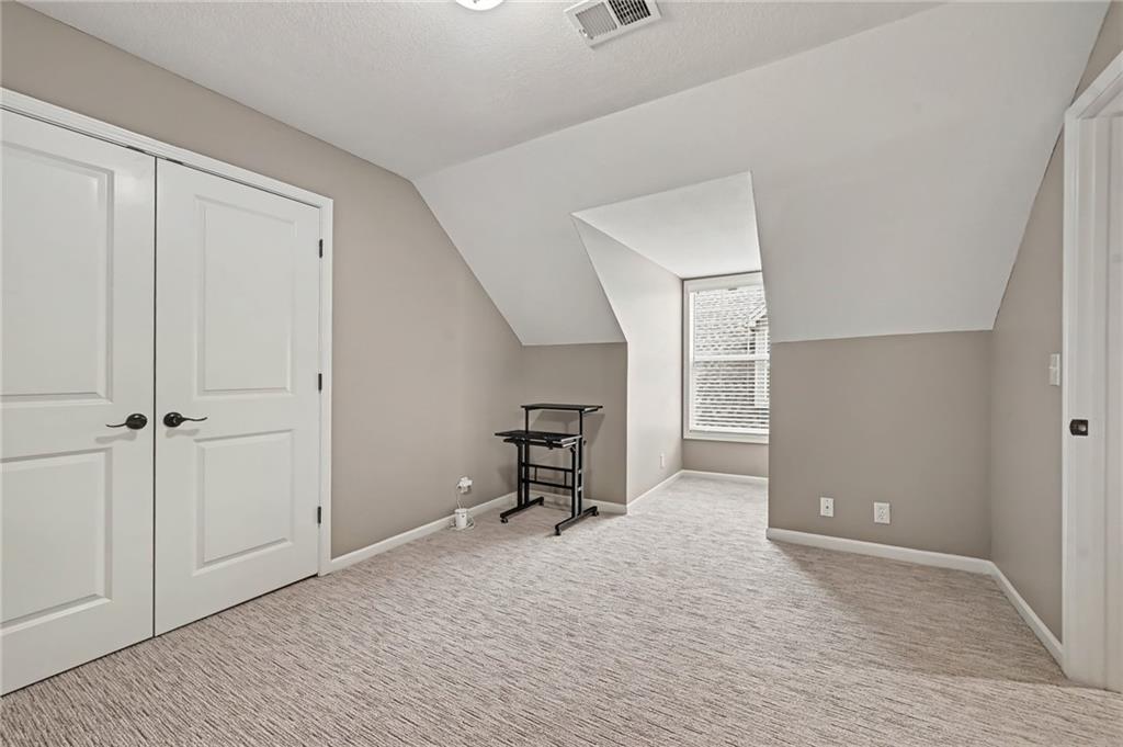 Unfurnished upstairs room with sloped ceilings, carpet, double closet doors, and a window.