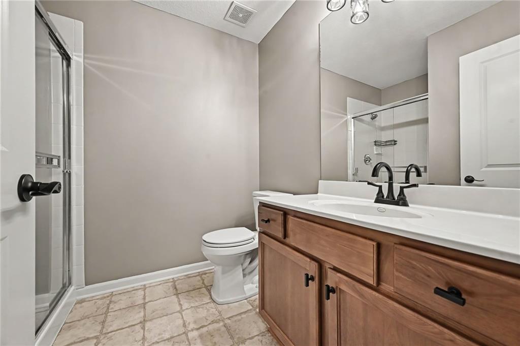 Bathroom with a wood vanity, white countertop, glass shower, and toilet.