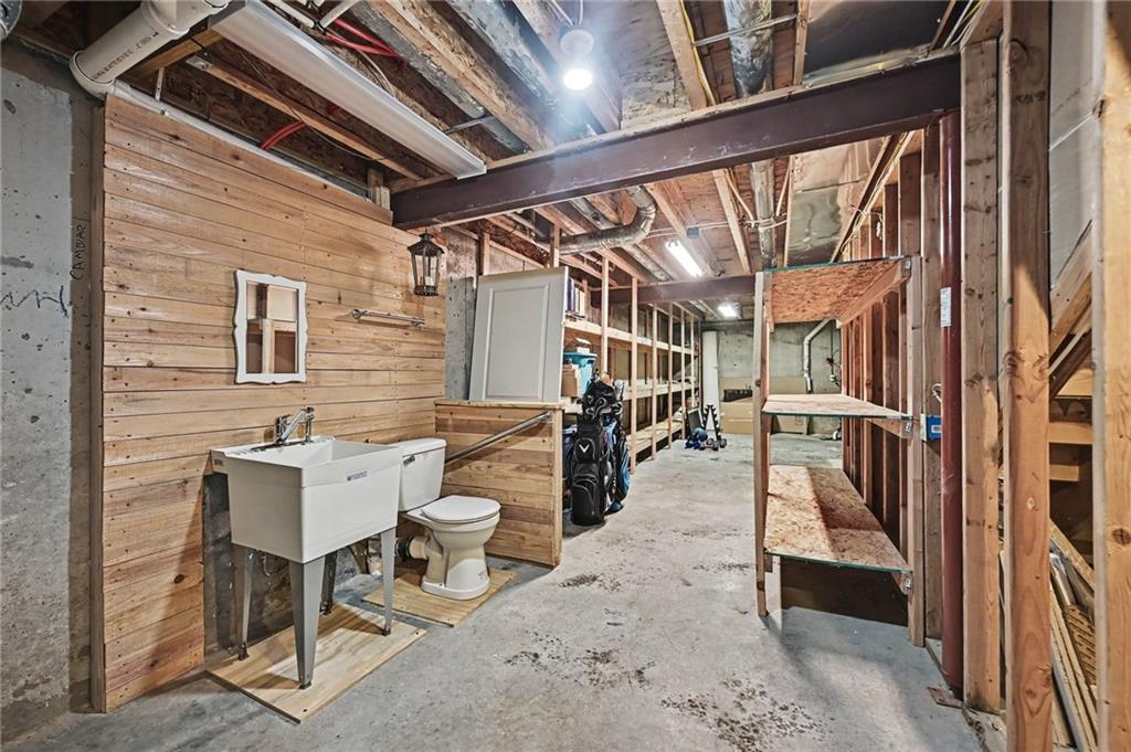 Unfinished basement with exposed framing, open shelves, and a sink and toilet.