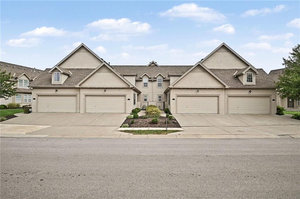 Beige attached homes with peaked gables, garage doors, and a landscaped walkway.