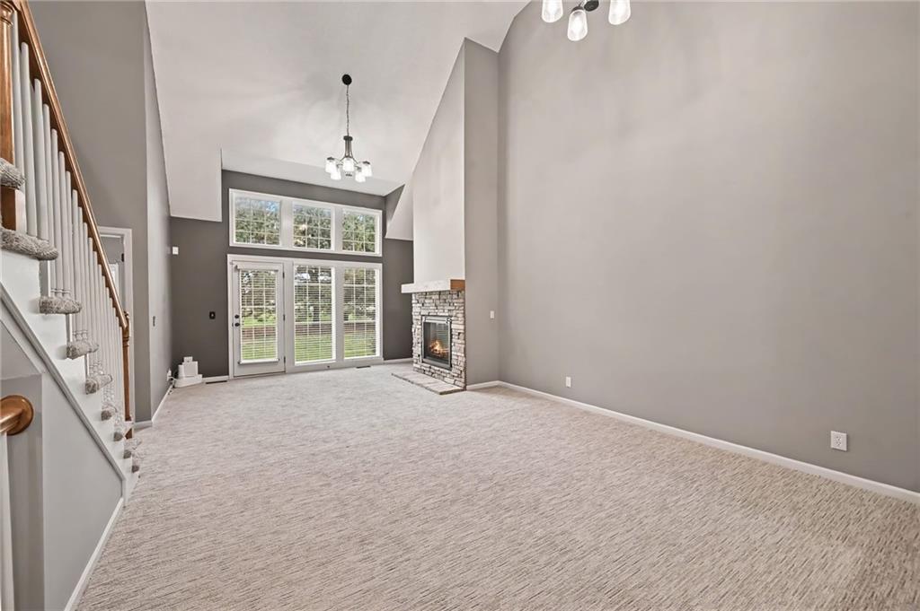 Unfurnished living room with a vaulted ceiling, stone fireplace, staircase, and tall windows.