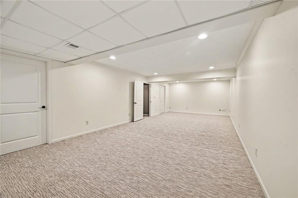 Empty finished basement room with light carpeting, recessed lights, and several doors.