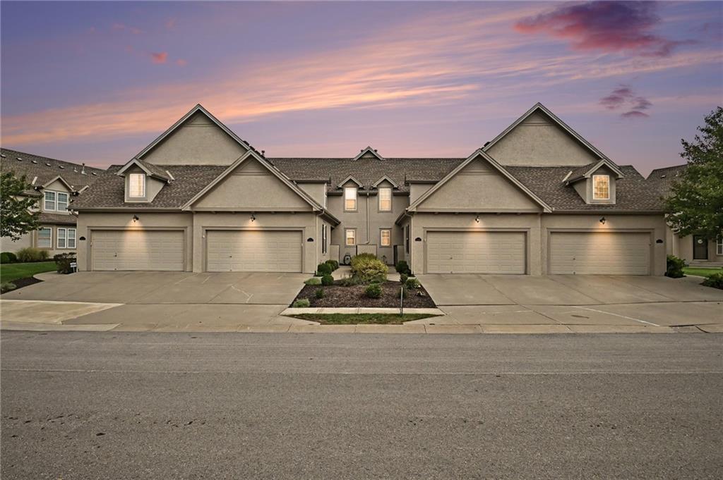 Attached home exterior with multiple garages and a landscaped entrance beneath a pink dusk sky.