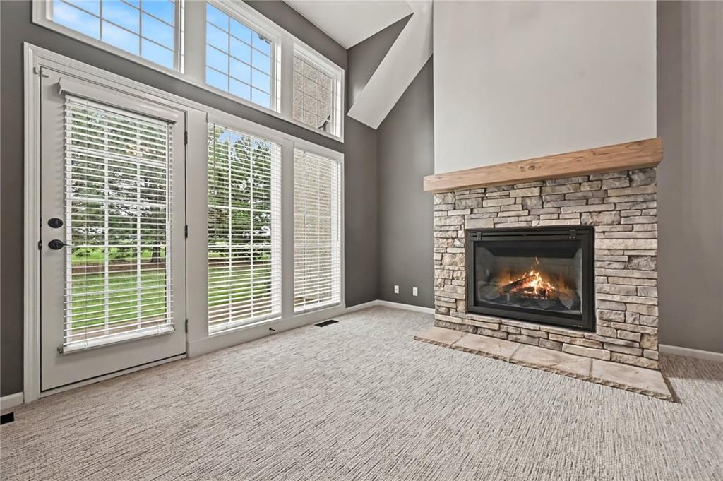 Empty living room with a vaulted ceiling, tall windows, and a stone fireplace with a wood mantel.