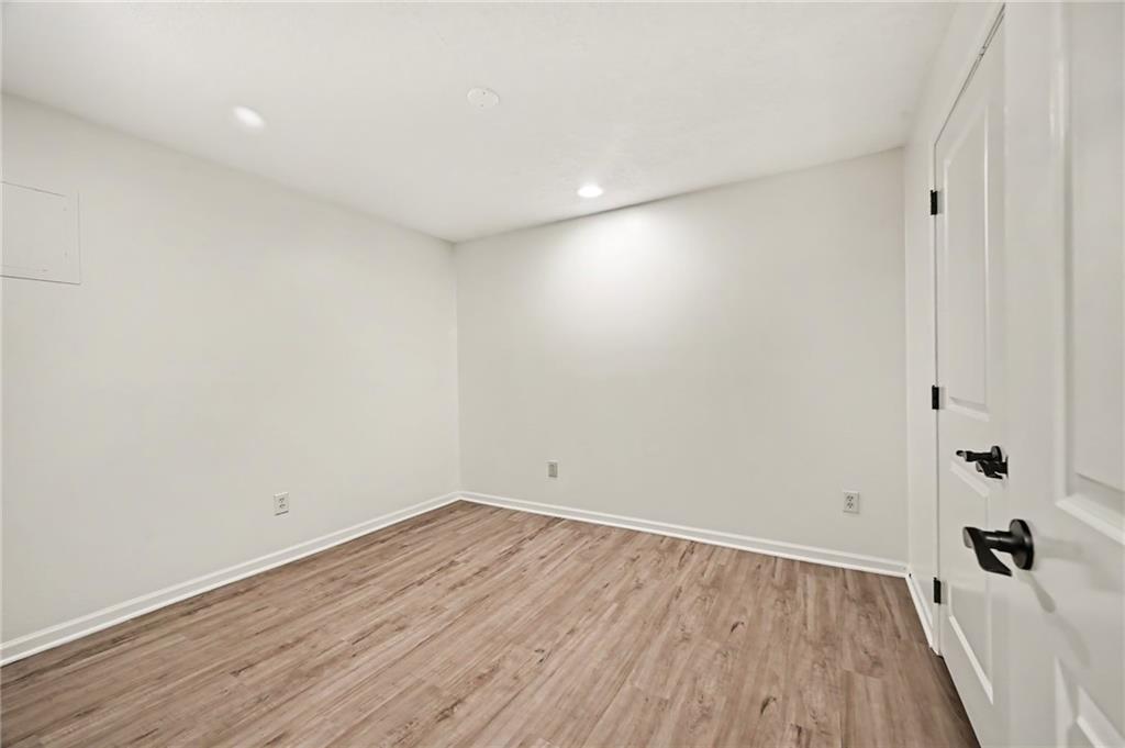 Empty room with wood-look plank flooring, white walls, and recessed ceiling lights.