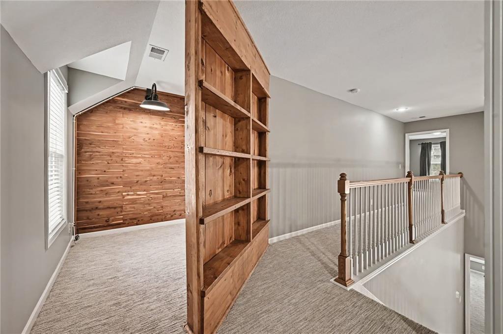 Carpeted loft landing with a built-in wooden bookcase, paneled accent wall, and white stair railing.