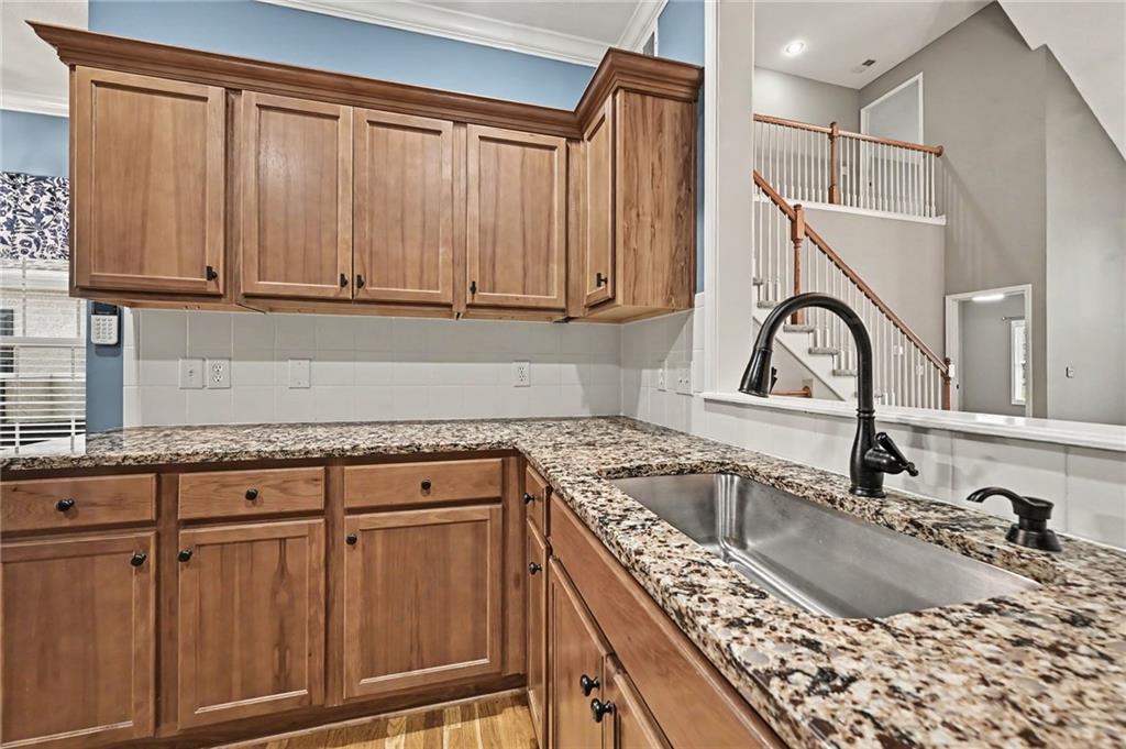 Kitchen with wood cabinets, granite counters, and a stainless-steel sink beside an open staircase.