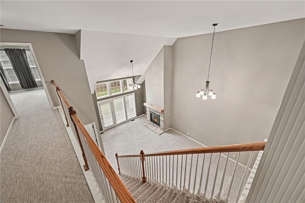 Carpeted living room with vaulted ceiling, stone fireplace, and upstairs overlook.
